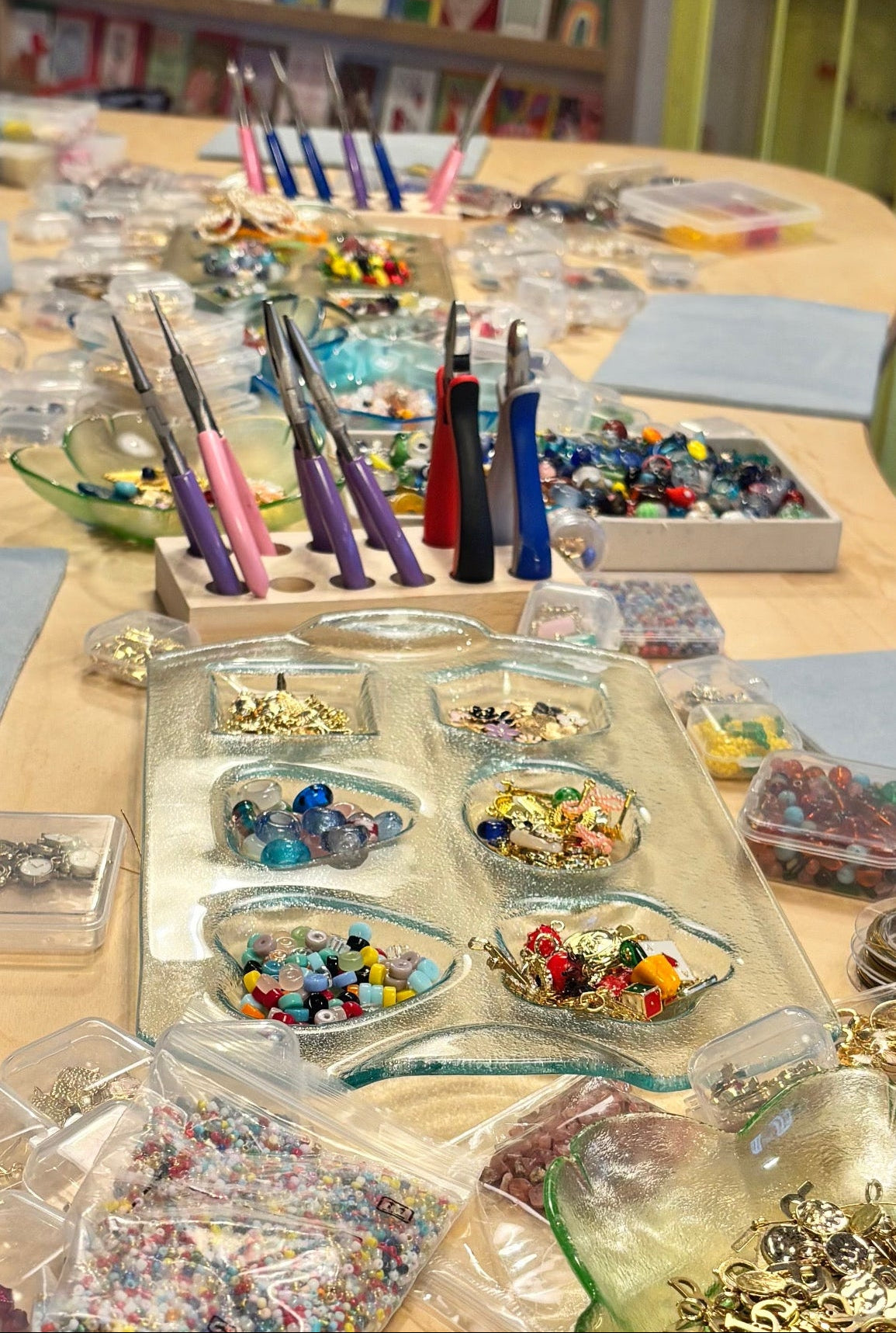 Table with jewelry-making supplies including beads and tools in a craft room setting.