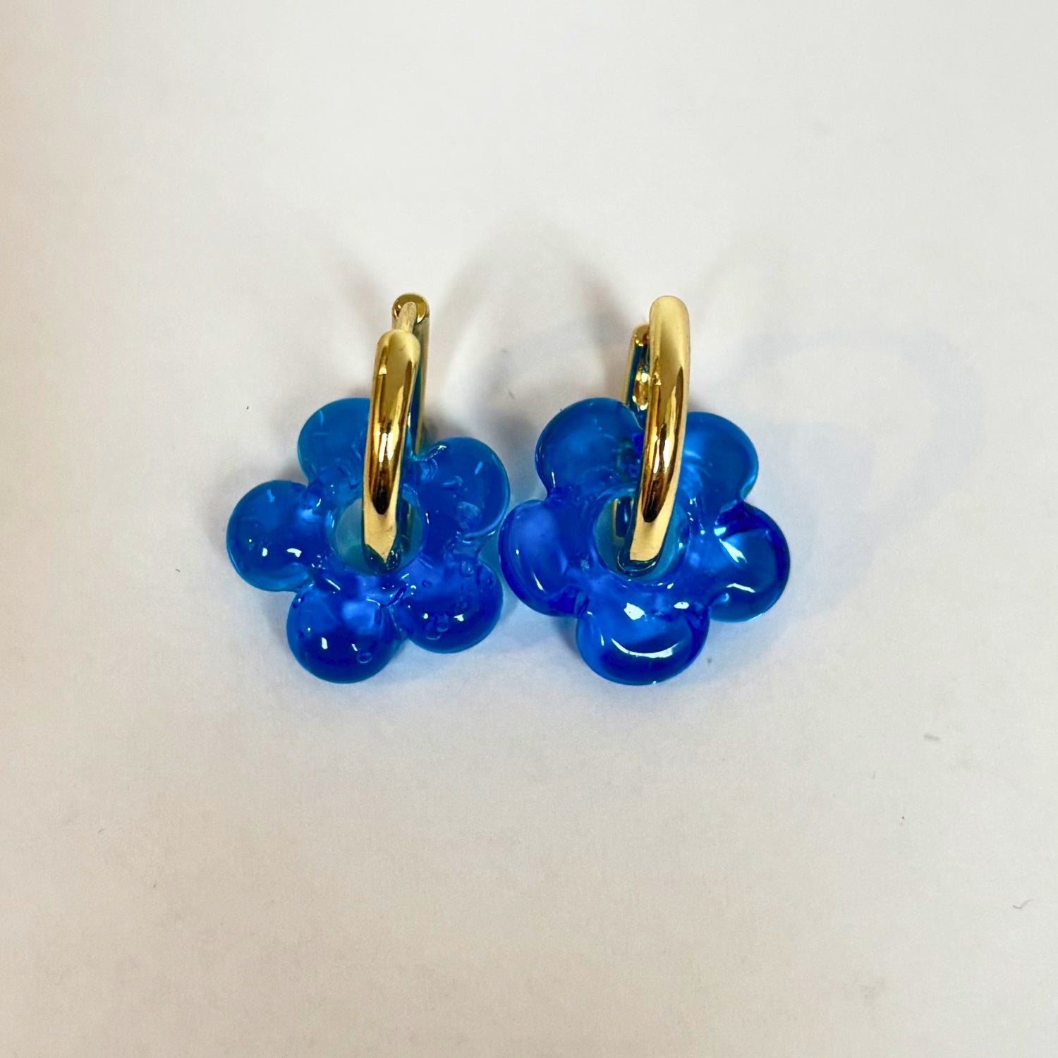 Blue flower-shaped earrings with gold loops on a white background