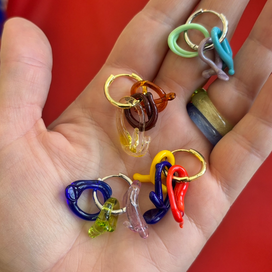 collection of mini melt colourful glass earrings on a hand against a red backgrounf