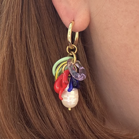 Close-up of a gold earring with colorful charms worn by a person with brown hair.
