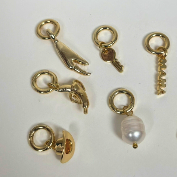 Gold charms including a hand, key, and pearl on a white background