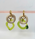 Pair of earrings with gold loops, beige circular middle pieces, and green open rings on a pink stand.