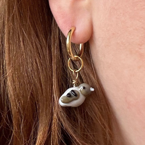 Gold hoop earring with a small bird charm worn by a person with red hair.