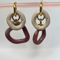 Pair of earrings with gold loops and ceramic rings on a pink stand against a white background