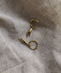 Two gold earrings on a textured beige fabric background