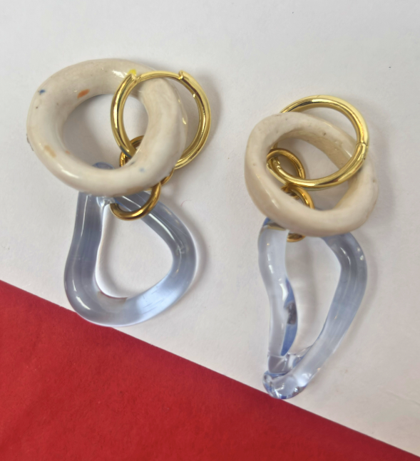 Pair of earrings with gold, beige, and clear design on a red and white background