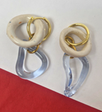 Pair of earrings with gold, beige, and clear design on a red and white background