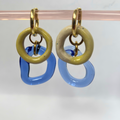 Pair of earrings with gold, beige, and blue circular designs on a white background