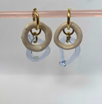 Pair of earrings with gold loops and beige circular stones on a clear stand against a light gray background.